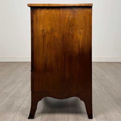 fig 3. A 20th-century mahogany serpentine cupboard featuring flame mahogany oval door panels, chevron veneering, a lower drawer with brass ring handles, and splayed bracket feet.