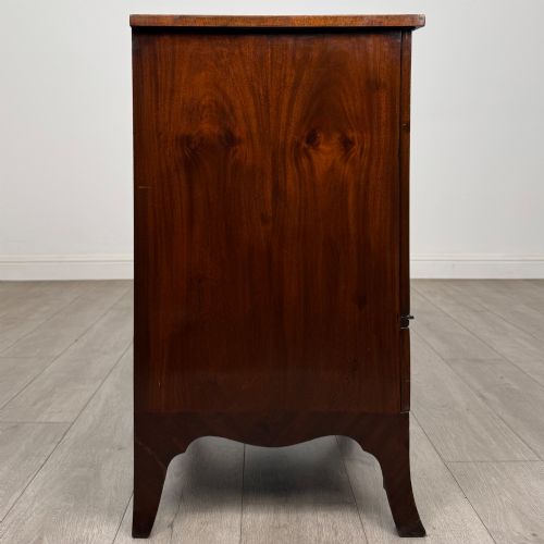 fig 7. A 20th-century mahogany serpentine cupboard featuring flame mahogany oval door panels, chevron veneering, a lower drawer with brass ring handles, and splayed bracket feet.
