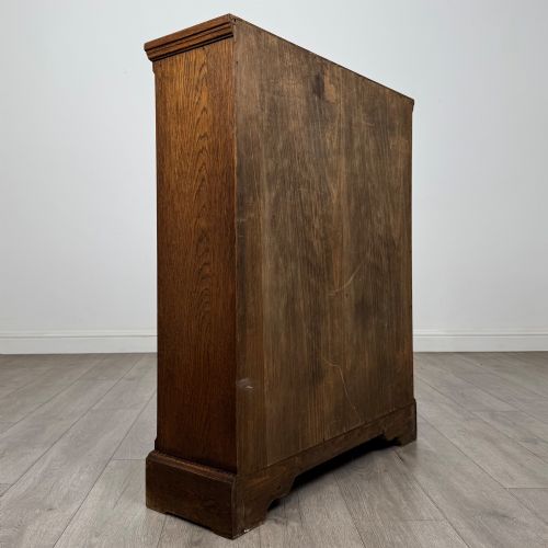 fig 5. A small medium-brown oak open bookcase featuring two upper shelves and a lower two-door cupboard with carved arched motifs and metal ring handles.