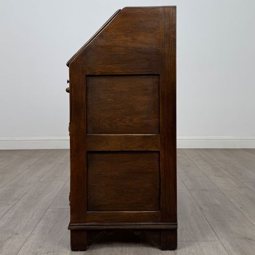 fig 3. A dark oak slant-front writing bureau featuring carved linenfold upper panels, a single carved drawer with wooden knobs, and a double-door cupboard base decorated with diamond lozenge carvings.