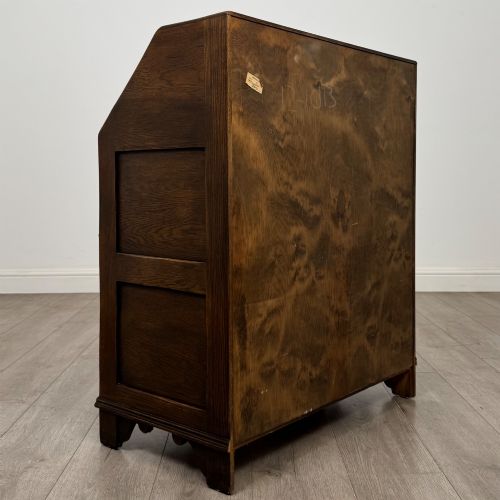 fig 4. A dark oak slant-front writing bureau featuring carved linenfold upper panels, a single carved drawer with wooden knobs, and a double-door cupboard base decorated with diamond lozenge carvings.