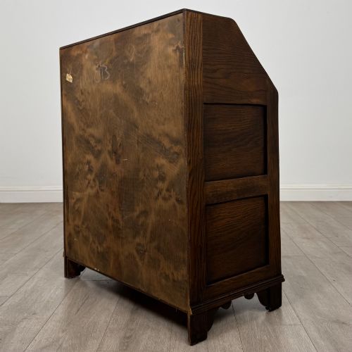 fig 6. A dark oak slant-front writing bureau featuring carved linenfold upper panels, a single carved drawer with wooden knobs, and a double-door cupboard base decorated with diamond lozenge carvings.