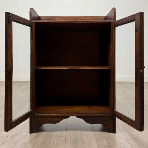 fig 1. An early 20th-century dark oak display cabinet featuring twin glazed doors, an interior shelf, and a gallery top.