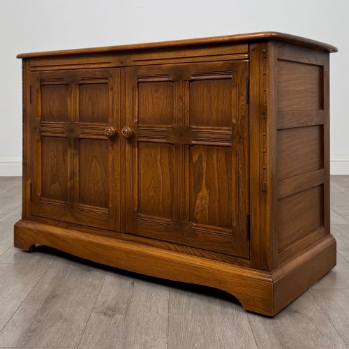 fig 2. A two-door golden oak storage cupboard featuring geometric panelled doors, turned timber knobs, and a low plinth base.