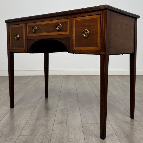 fig 1. An Edwardian mahogany writing table featuring three drawers with satinwood crossbanding, brass ring pull handles, and square tapered legs.