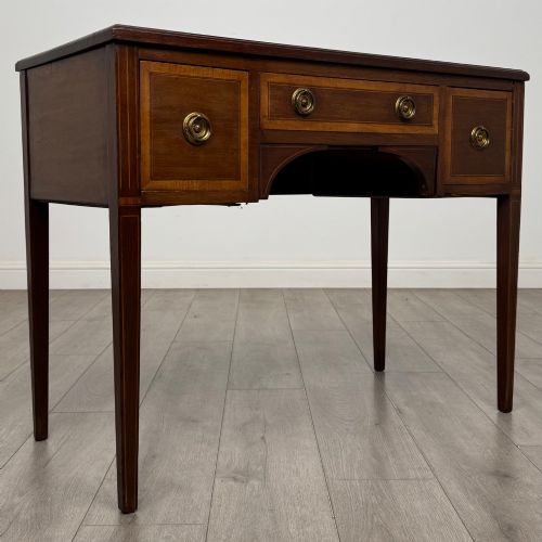 fig 7. An Edwardian mahogany writing table featuring three drawers with satinwood crossbanding, brass ring pull handles, and square tapered legs.
