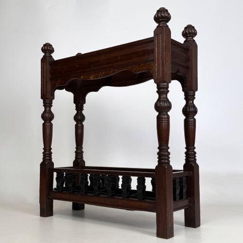 fig 1. An Edwardian dark oak umbrella stand featuring four turned corner posts topped with finials, a shaped upper crossbar, and a lower spindle gallery enclosing a drip tray.