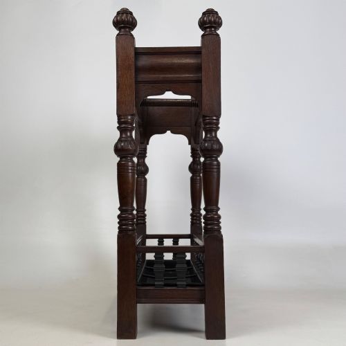 fig 2. An Edwardian dark oak umbrella stand featuring four turned corner posts topped with finials, a shaped upper crossbar, and a lower spindle gallery enclosing a drip tray.