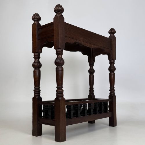 fig 3. An Edwardian dark oak umbrella stand featuring four turned corner posts topped with finials, a shaped upper crossbar, and a lower spindle gallery enclosing a drip tray.