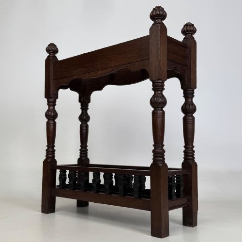 fig 5. An Edwardian dark oak umbrella stand featuring four turned corner posts topped with finials, a shaped upper crossbar, and a lower spindle gallery enclosing a drip tray.