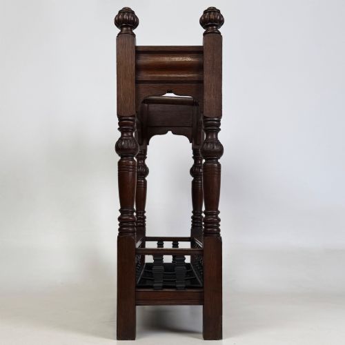 fig 6. An Edwardian dark oak umbrella stand featuring four turned corner posts topped with finials, a shaped upper crossbar, and a lower spindle gallery enclosing a drip tray.