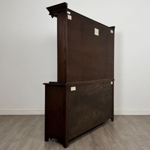 fig 5. A dark oak display cabinet with a leaded glass central upper cupboard, flanked by open shelves, set atop a lower unit with multiple drawers and carved cupboard doors.