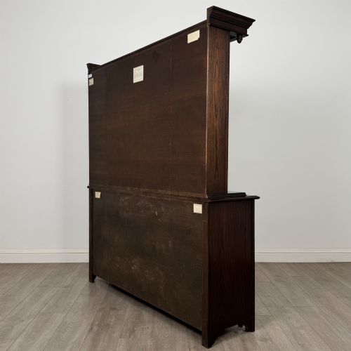 fig 7. A dark oak display cabinet with a leaded glass central upper cupboard, flanked by open shelves, set atop a lower unit with multiple drawers and carved cupboard doors.