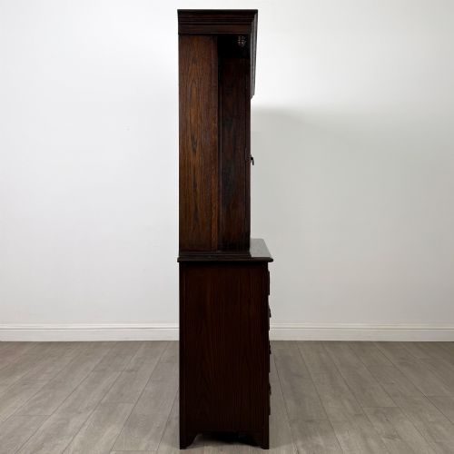 fig 8. A dark oak display cabinet with a leaded glass central upper cupboard, flanked by open shelves, set atop a lower unit with multiple drawers and carved cupboard doors.