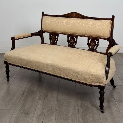 fig 1. An antique Victorian rosewood settee featuring central backrest marquetry inlay, open armrests, turned front legs on castors, and cream damask upholstery.