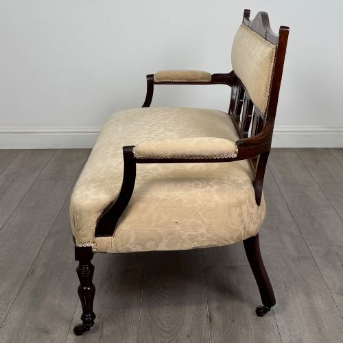 fig 2. An antique Victorian rosewood settee featuring central backrest marquetry inlay, open armrests, turned front legs on castors, and cream damask upholstery.