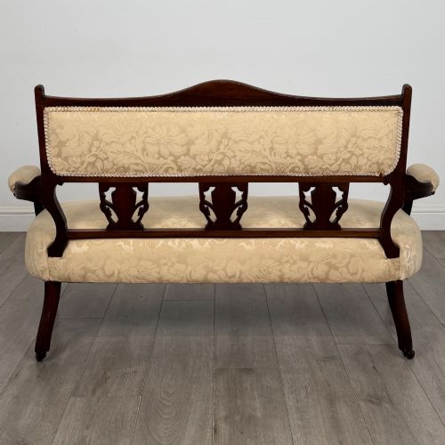 fig 4. An antique Victorian rosewood settee featuring central backrest marquetry inlay, open armrests, turned front legs on castors, and cream damask upholstery.