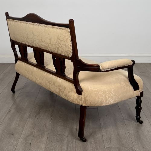 fig 5. An antique Victorian rosewood settee featuring central backrest marquetry inlay, open armrests, turned front legs on castors, and cream damask upholstery.