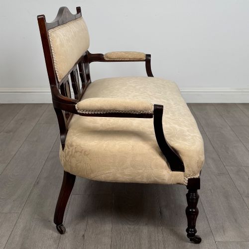 fig 6. An antique Victorian rosewood settee featuring central backrest marquetry inlay, open armrests, turned front legs on castors, and cream damask upholstery.