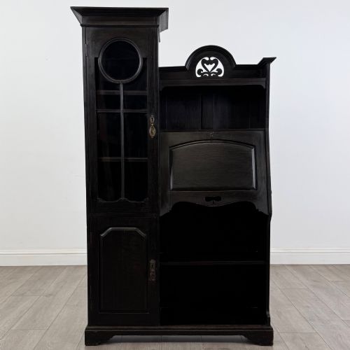 fig 1. An ebonised oak bureau bookcase featuring an asymmetrical design with a glazed door cabinet, a slanted fall-front writing surface, open shelving, and a heart cutout crest.