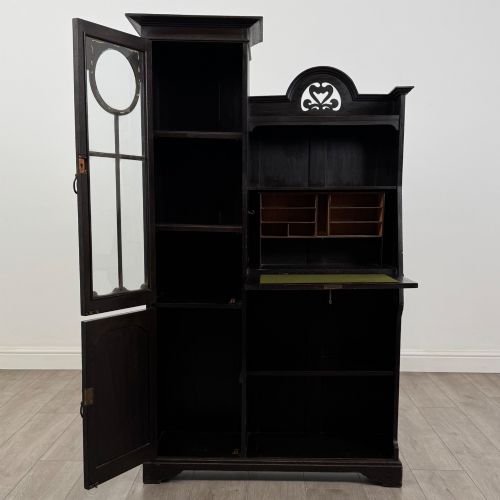 fig 2. An ebonised oak bureau bookcase featuring an asymmetrical design with a glazed door cabinet, a slanted fall-front writing surface, open shelving, and a heart cutout crest.