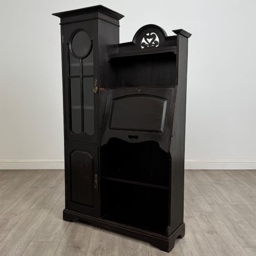fig 3. An ebonised oak bureau bookcase featuring an asymmetrical design with a glazed door cabinet, a slanted fall-front writing surface, open shelving, and a heart cutout crest.