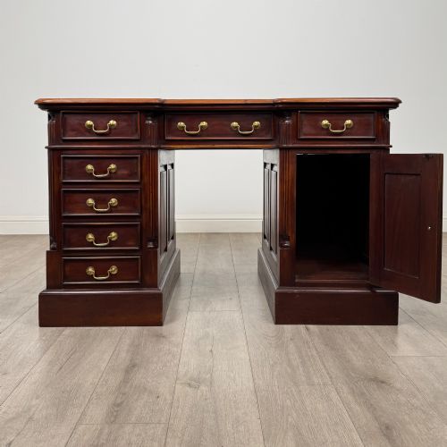 fig 1. A dark mahogany pedestal desk featuring a central kneehole drawer flanked by five drawers on the left and a panelled cupboard door on the right, all fitted with brass drop handles.