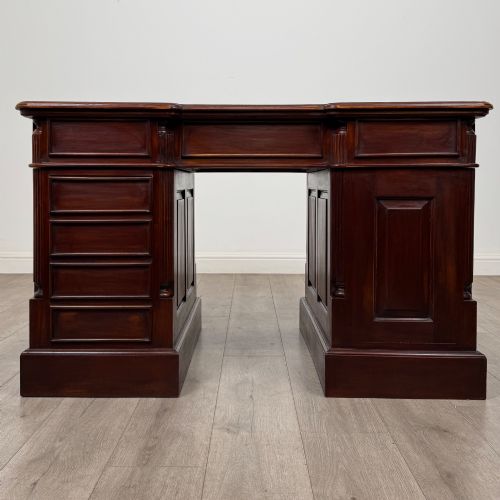 fig 5. A dark mahogany pedestal desk featuring a central kneehole drawer flanked by five drawers on the left and a panelled cupboard door on the right, all fitted with brass drop handles.