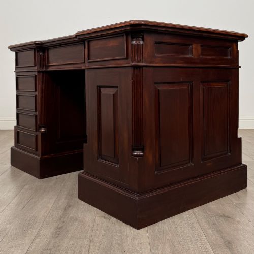 fig 6. A dark mahogany pedestal desk featuring a central kneehole drawer flanked by five drawers on the left and a panelled cupboard door on the right, all fitted with brass drop handles.