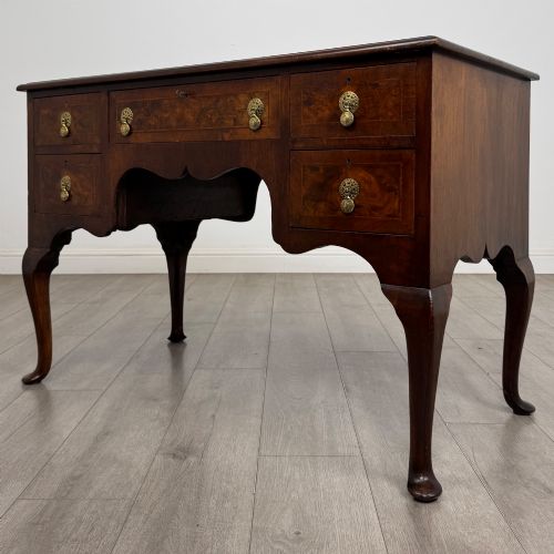 fig 1. A 19th-century Victorian writing table crafted from burr walnut with five drawer fronts, ornate brass drop handles, a shaped central kneehole, and cabriole legs.