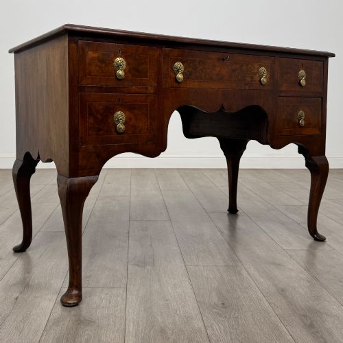 fig 7. A 19th-century Victorian writing table crafted from burr walnut with five drawer fronts, ornate brass drop handles, a shaped central kneehole, and cabriole legs.