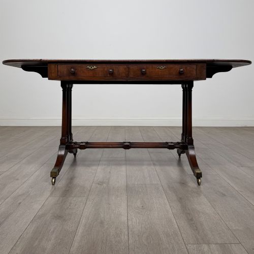 fig 1. A 19th-century Regency style yew wood side table featuring drop-leaf ends, twin drawers with brass escutcheons and round knobs, turned twin-stem supports, a stretcher, and brass castors.