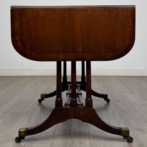 fig 3. A 19th-century Regency style yew wood side table featuring drop-leaf ends, twin drawers with brass escutcheons and round knobs, turned twin-stem supports, a stretcher, and brass castors.