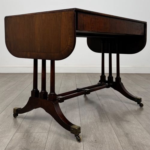 fig 4. A 19th-century Regency style yew wood side table featuring drop-leaf ends, twin drawers with brass escutcheons and round knobs, turned twin-stem supports, a stretcher, and brass castors.