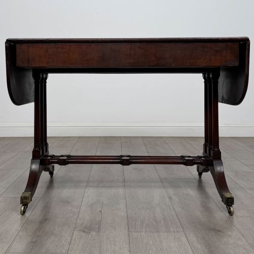 fig 5. A 19th-century Regency style yew wood side table featuring drop-leaf ends, twin drawers with brass escutcheons and round knobs, turned twin-stem supports, a stretcher, and brass castors.