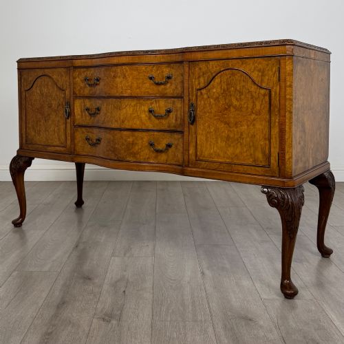 fig 2. An Edwardian burr walnut sideboard featuring three central drawers flanked by two cupboard doors, set on carved cabriole legs.