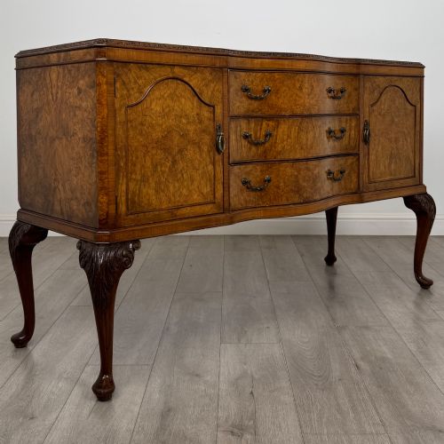 fig 8. An Edwardian burr walnut sideboard featuring three central drawers flanked by two cupboard doors, set on carved cabriole legs.