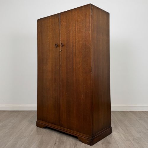 fig 2. A freestanding mid-20th-century double wardrobe crafted from medium brown oak with twin flush doors, small circular wooden handles, and a low plinth base.