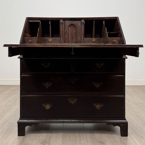fig 1. An 18th-century dark oak Georgian bureau with a slant-front writing slope, brass batwing drop handles, and bracket feet.