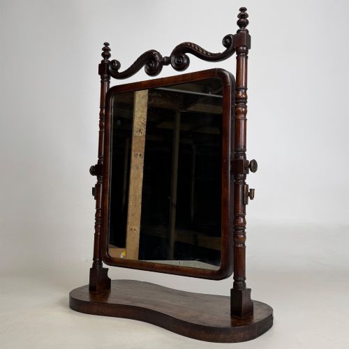 fig 2. A 19th-century mahogany dressing mirror with turned side columns, carved scrollwork cresting, and an adjustable rectangular glass frame on a shaped base.