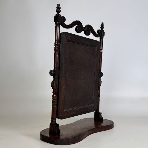 fig 5. A 19th-century mahogany dressing mirror with turned side columns, carved scrollwork cresting, and an adjustable rectangular glass frame on a shaped base.