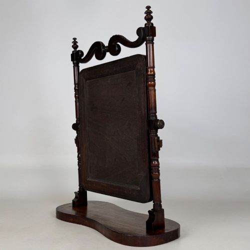 fig 7. A 19th-century mahogany dressing mirror with turned side columns, carved scrollwork cresting, and an adjustable rectangular glass frame on a shaped base.