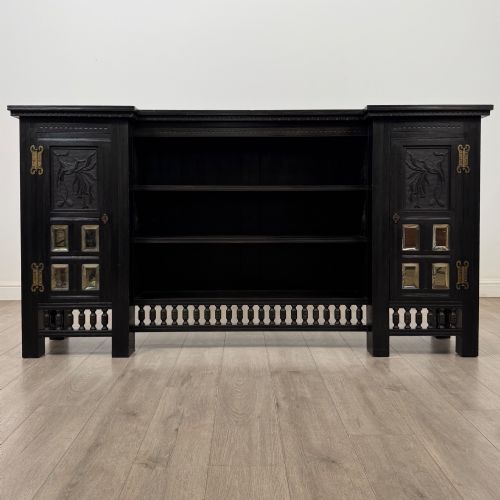 fig 1. An antique ebonised black wood sideboard featuring a central open bookshelf, two carved side doors with glass panels, brass hardware, and a spindled lower rail.