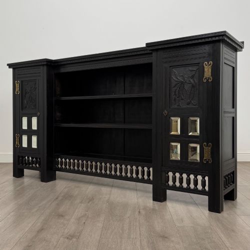 fig 3. An antique ebonised black wood sideboard featuring a central open bookshelf, two carved side doors with glass panels, brass hardware, and a spindled lower rail.