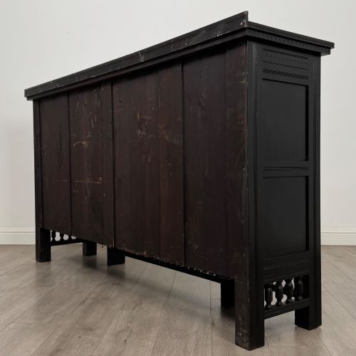fig 7. An antique ebonised black wood sideboard featuring a central open bookshelf, two carved side doors with glass panels, brass hardware, and a spindled lower rail.