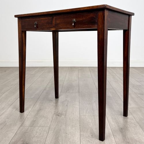 fig 1. An antique dark oak Edwardian side table with two front drawers, metallic drop handles, and straight tapered legs.