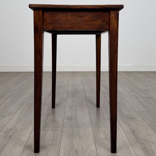 fig 6. An antique dark oak Edwardian side table with two front drawers, metallic drop handles, and straight tapered legs.