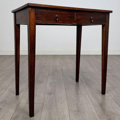 fig 7. An antique dark oak Edwardian side table with two front drawers, metallic drop handles, and straight tapered legs.