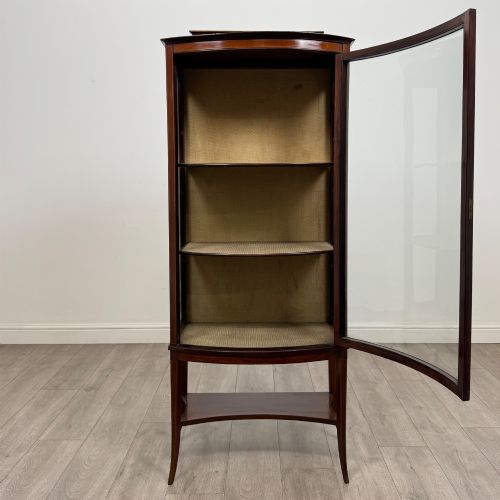 fig 1. An Edwardian mahogany display cabinet with a bow-front glazed door, fabric-lined interior shelves, marquetry inlay, and slender tapered legs with a lower shelf.