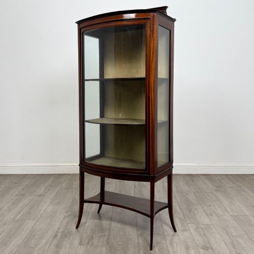 fig 2. An Edwardian mahogany display cabinet with a bow-front glazed door, fabric-lined interior shelves, marquetry inlay, and slender tapered legs with a lower shelf.